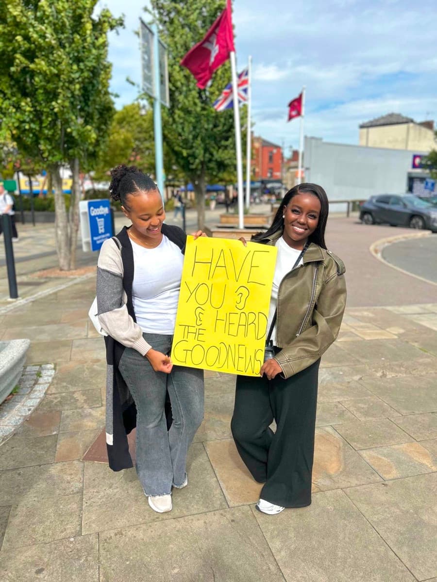 Two young women holding a sign asking if people have heard the good news